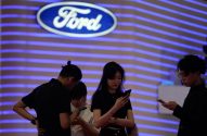 Quatro pessoas em frente ao logo da Ford, parede com luzes azuis, todas usando celulares.