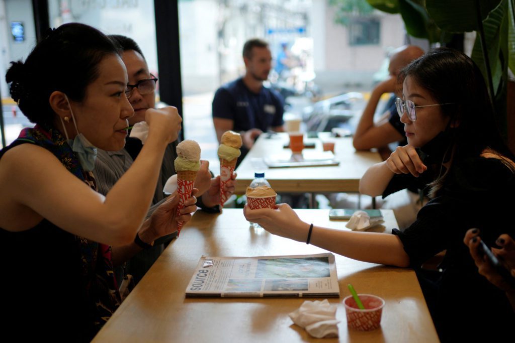 Duas mulheres comem sorvete em casquinha e conversam em cafeteria.