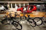 Bicicletas em primeiro plano, com carro vermelho em linha de montagem em uma fábrica.
