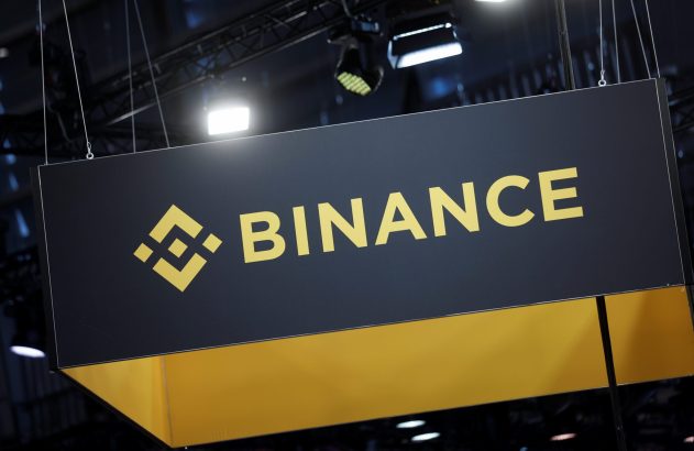Letreiro suspenso preto e amarelo da Binance, com seu logo e nome.