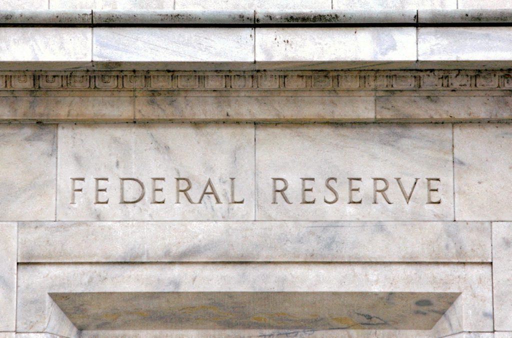 Nome "FEDERAL RESERVE" gravado na fachada de mármore de um edifício, com detalhes arquitetônicos.