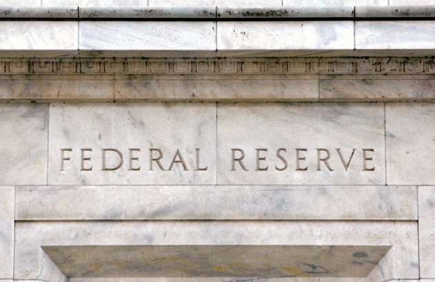 Nome "FEDERAL RESERVE" gravado na fachada de mármore de um edifício, com detalhes arquitetônicos.