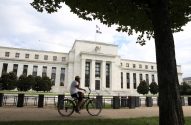 Ciclista em frente ao Federal Reserve, edifício branco com colunas e bandeiras dos EUA.