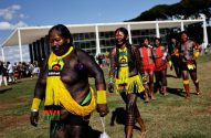 Grupo de indígenas com vestimentas tradicionais e pinturas corporais caminha em frente a um edifício governamental.