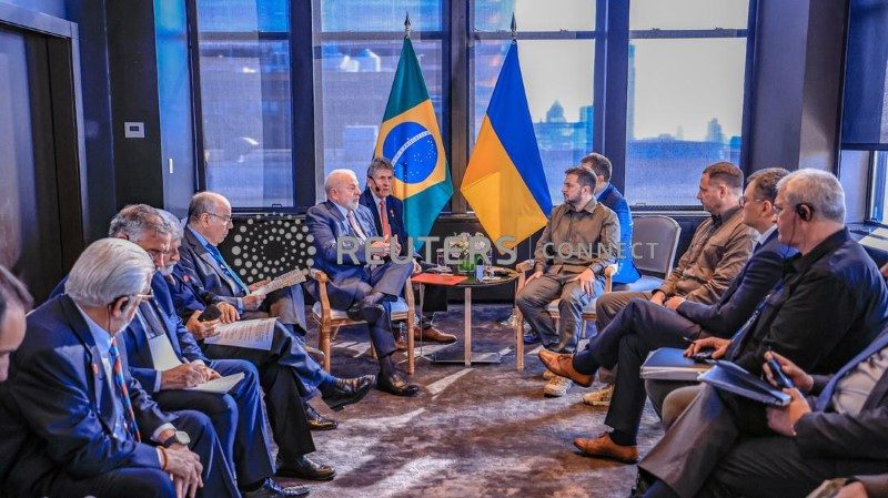 Presidentes Lula (Brasil) e Zelensky (Ucrânia) em reunião, com bandeiras dos seus países ao fundo.