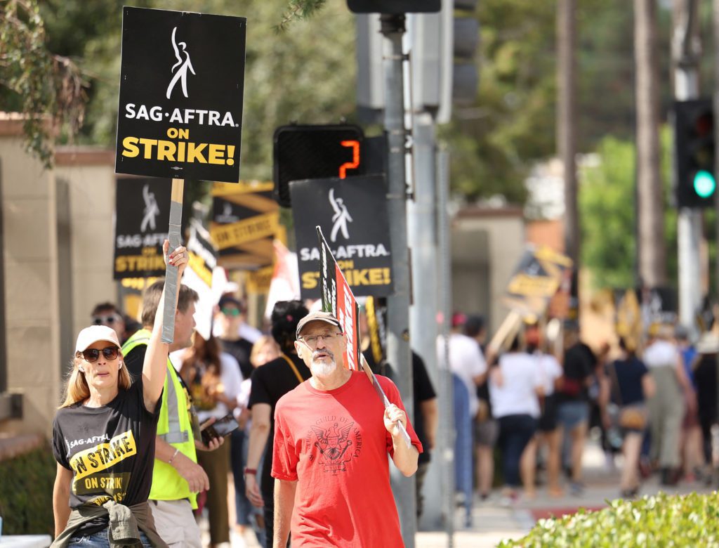 Pessoas em greve da SAG-AFTRA seguram cartazes "ON STRIKE!" em protesto ao ar livre.