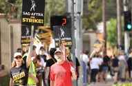 Pessoas em greve da SAG-AFTRA seguram cartazes "ON STRIKE!" em protesto ao ar livre.