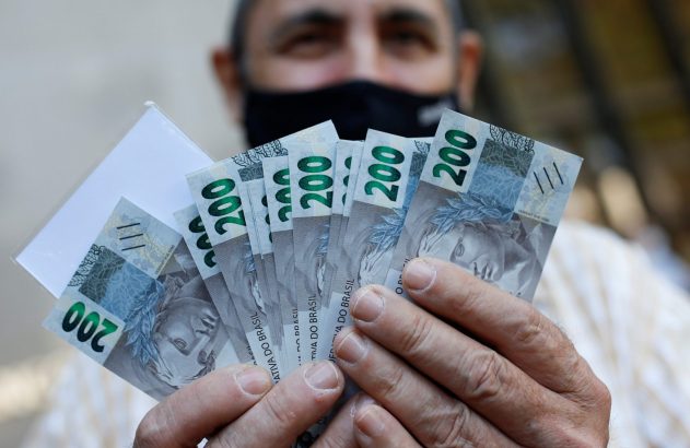 Homem de máscara segurando um leque de notas de 200 reais, estendidas para a frente.