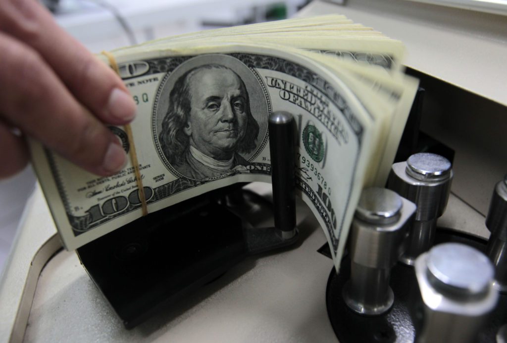 Mão alimentando ou removendo maço de notas de 100 dólares em máquina de contar dinheiro.