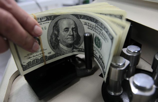 Mão alimentando ou removendo maço de notas de 100 dólares em máquina de contar dinheiro.