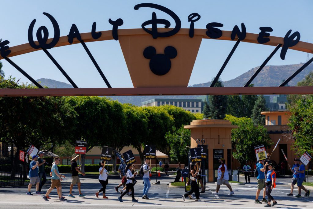 Pessoas caminhando sob o letreiro "Walt Disney" e logo do Mickey na entrada.