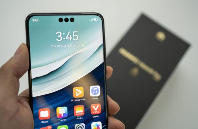 Mão segura smartphone com entalhe, exibindo tela com 3:45, data e apps como "HUAWEI Video" e "Music".