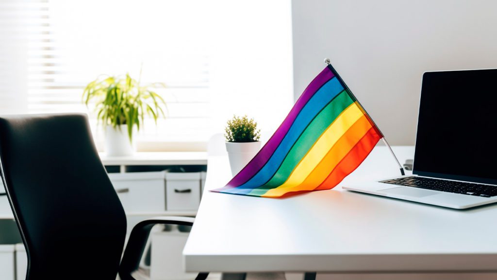 Bandeira do orgulho LGBTQIA+ em mesa de escritório com laptop.