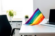 Bandeira do orgulho LGBTQIA+ em mesa de escritório com laptop.