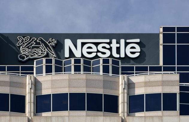 Prédio da Nestlé com seu logo, exibindo o nome e o símbolo de pássaros em um ninho, sob céu azul.