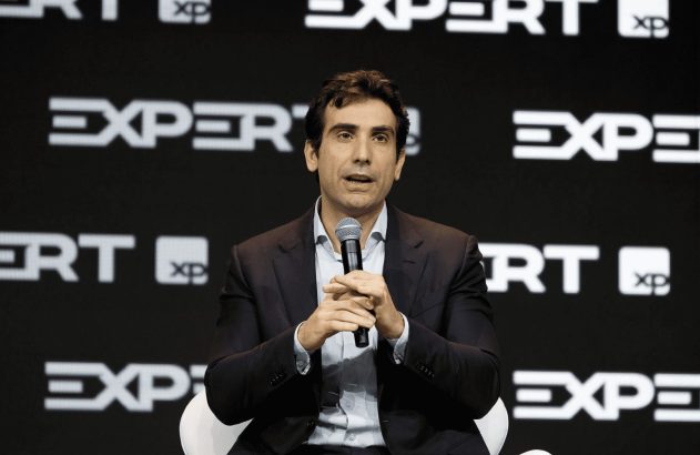 Homem de terno sentado falando ao microfone. Fundo preto com "EXPERT" e "XP".