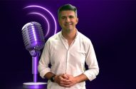 Homem sorrindo com microfone roxo vintage à esquerda e anéis luminosos em fundo roxo escuro.