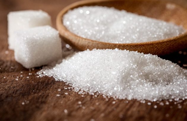 Açúcar granulado e em cubos, com colher de pau sobre superfície de madeira.