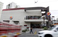Prédio do Burger King em rua movimentada. Veículos borrados em velocidade e pessoa caminhando na calçada.