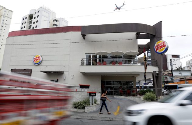 Prédio do Burger King em rua movimentada. Veículos borrados em velocidade e pessoa caminhando na calçada.