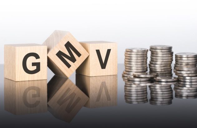 cubos de madeira formando a sigla "GMV" ao lado de 3 pilhas de moeda