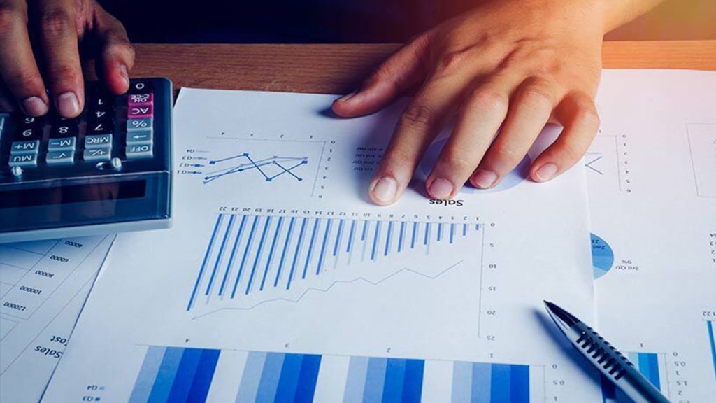 Mãos usando calculadora e gráficos em uma análise financeira.
