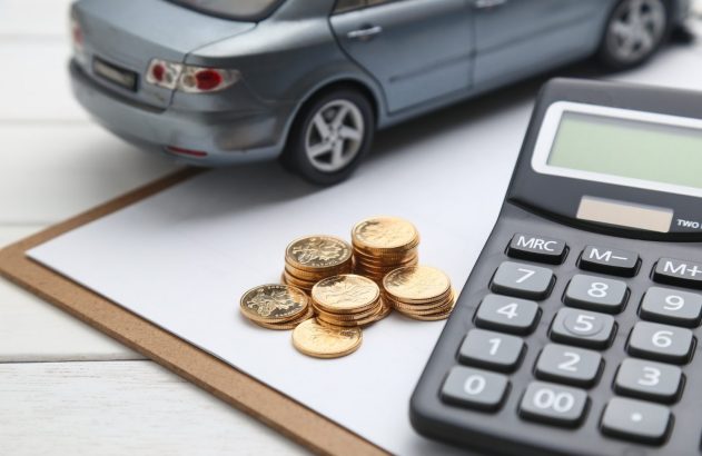 miniatura de um carro ao lado de uma pilha de moedas e uma calculadora, com uma prancheta embaixo. A imagem ilustra o ITCMD