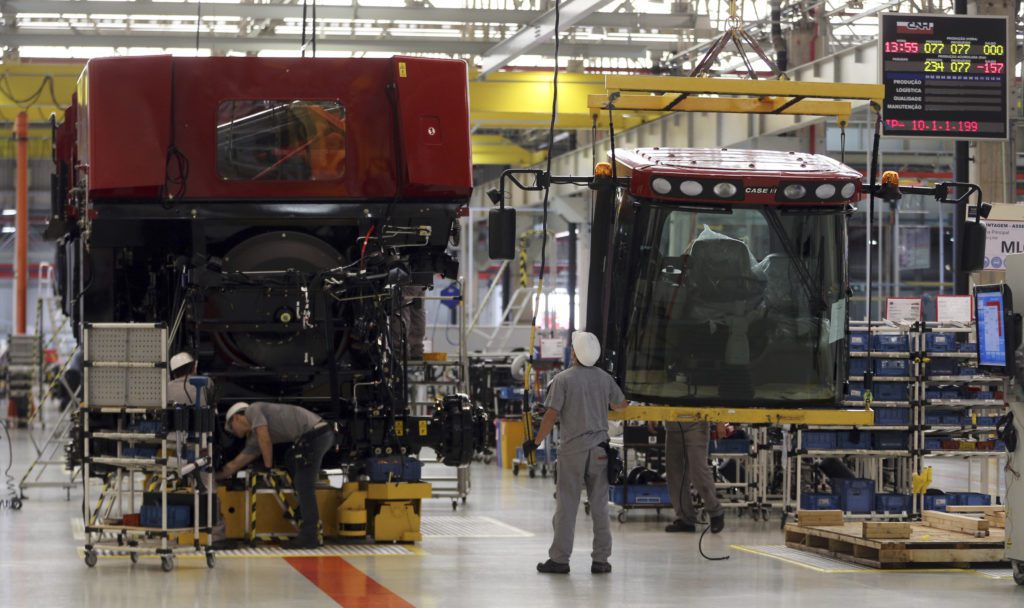 Operários montam grandes máquinas agrícolas vermelhas em uma linha de produção. Uma cabine Case IH é içada sobre o chassi.