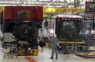 Operários montam grandes máquinas agrícolas vermelhas em uma linha de produção. Uma cabine Case IH é içada sobre o chassi.