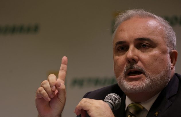 Homem grisalho e barbudo fala ao microfone, com o dedo indicador levantado.