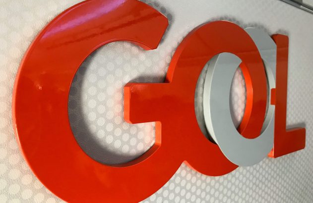 Logo 3D GOL brilhante. Letras laranja e cinza em relevo sobre parede com pontos.