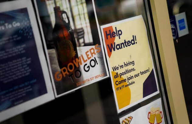 Placa "Help Wanted!" em vitrine de loja, indicando "Estamos contratando todas as posições."