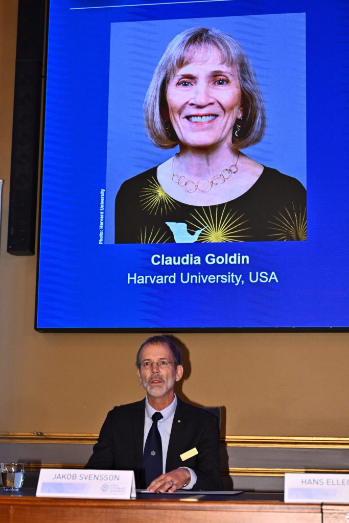 Jakob Svensson fala em mesa. Tela atrás exibe foto de Claudia Goldin, Harvard University, USA.