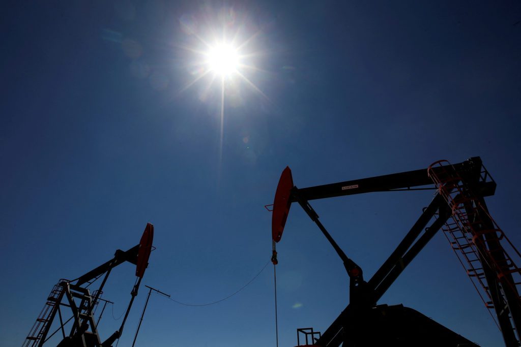 Duas bombas de petróleo em silhueta sob sol forte em céu azul.