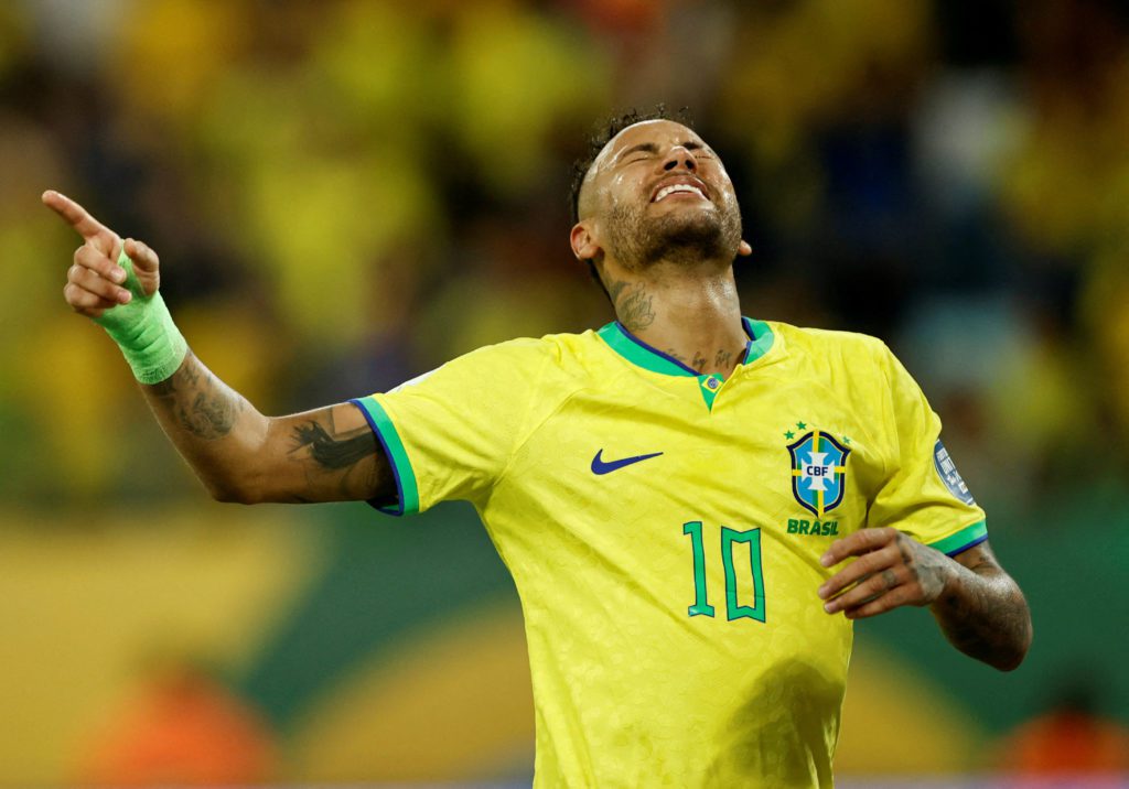 Jogador com camisa 10 do Brasil, em êxtase, apontando para cima com braço enfaixado.