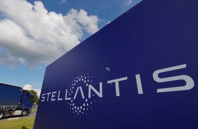 Sinal azul da Stellantis com logo branco. Caminhão azul e céu com nuvens ao fundo.