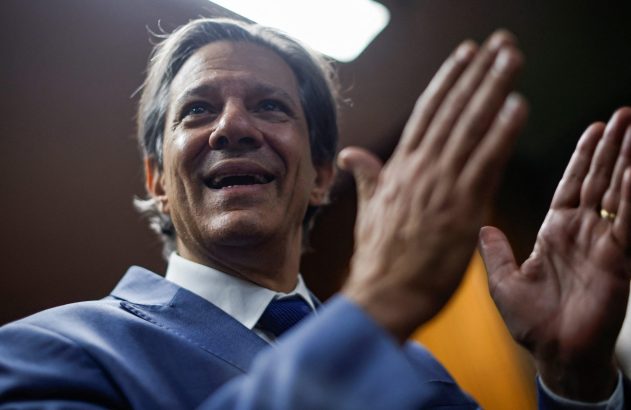 Homem de terno azul sorrindo e aplaudindo com as mãos levantadas.