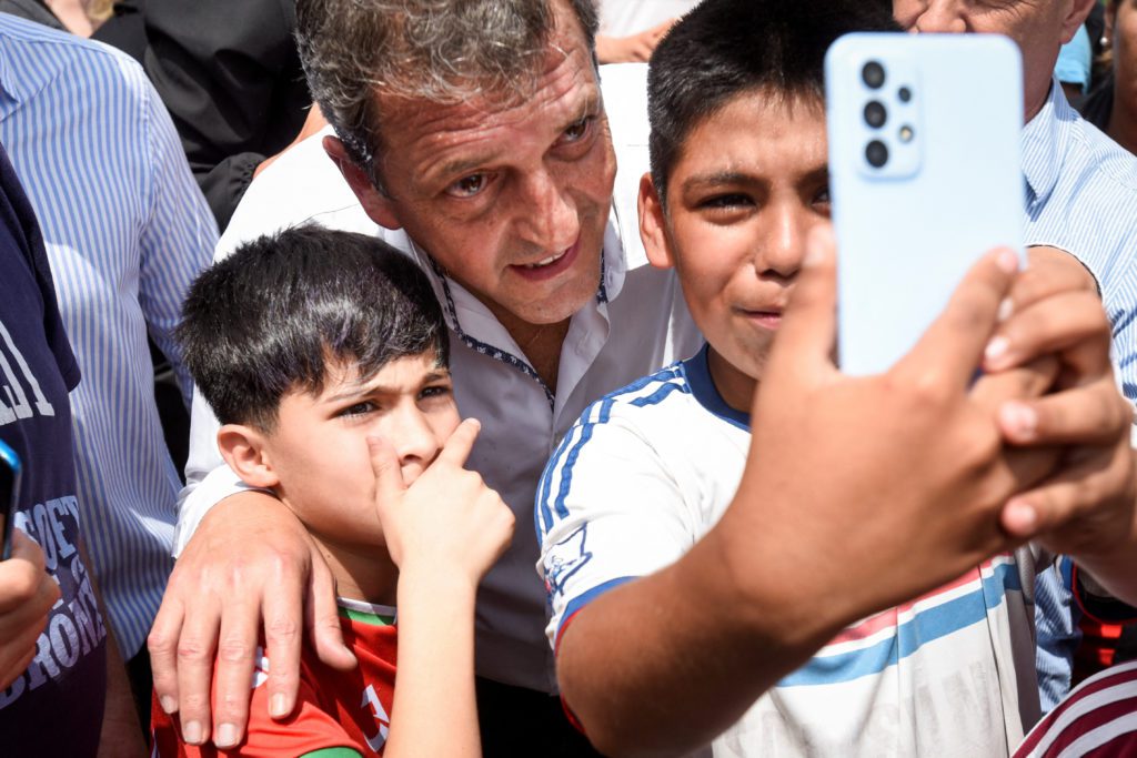 Homem e dois meninos posam para selfie; um deles segura o celular.