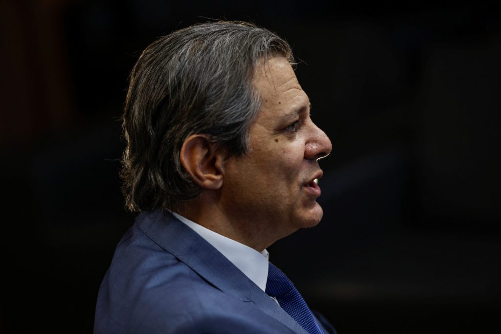 Homem de terno em perfil, boca aberta como se falasse. Cabelo grisalho. Fundo escuro.