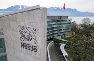 Sede da Nestlé com seu logo em destaque, bandeira da Suíça, lago e montanhas nevadas ao fundo.