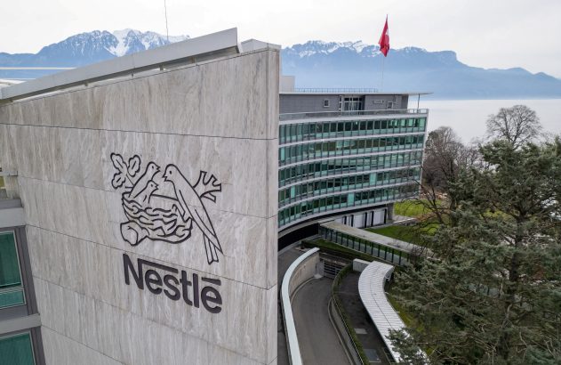 Sede da Nestlé com seu logo em destaque, bandeira da Suíça, lago e montanhas nevadas ao fundo.
