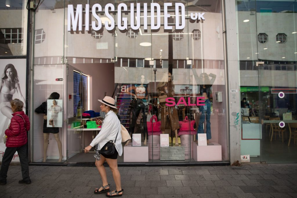 Mulher passa por loja Missguided com letreiro "SALE" na vitrine.