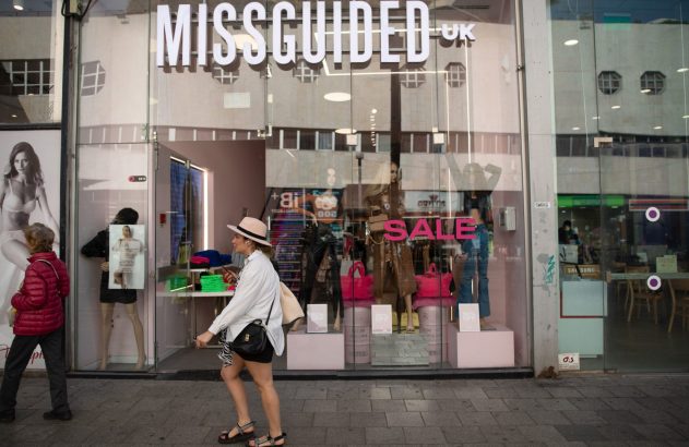 Mulher passa por loja Missguided com letreiro "SALE" na vitrine.