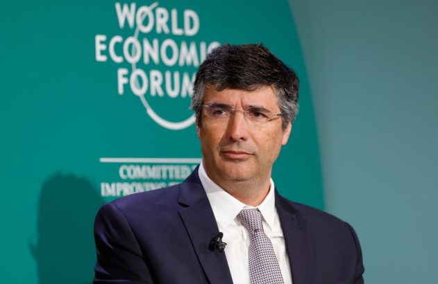 André Esteves está de terno preto, gravata cinza, olhando para o lado
