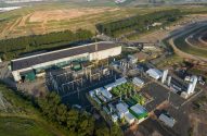Vista aérea de planta industrial com edifícios, tubulações e tanques em meio a campos e estradas.