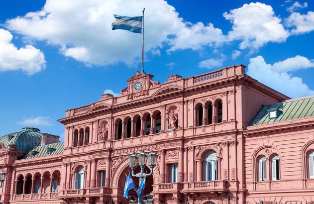 Casa Rosada, palácio presidencial da Argentina, sob céu azul com nuvens e a bandeira argentina ao alto.
