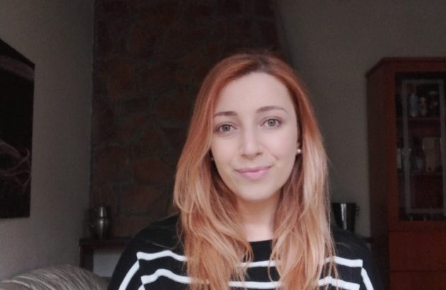 Mulher de camisa listrada preta e branca sorrindo para a câmera, em ambiente interno.