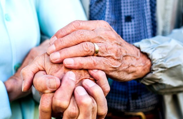 Mãos envelhecidas de um casal se segurando. Uma mão cobre a outra, transmitindo carinho e apoio. Imposto de renda