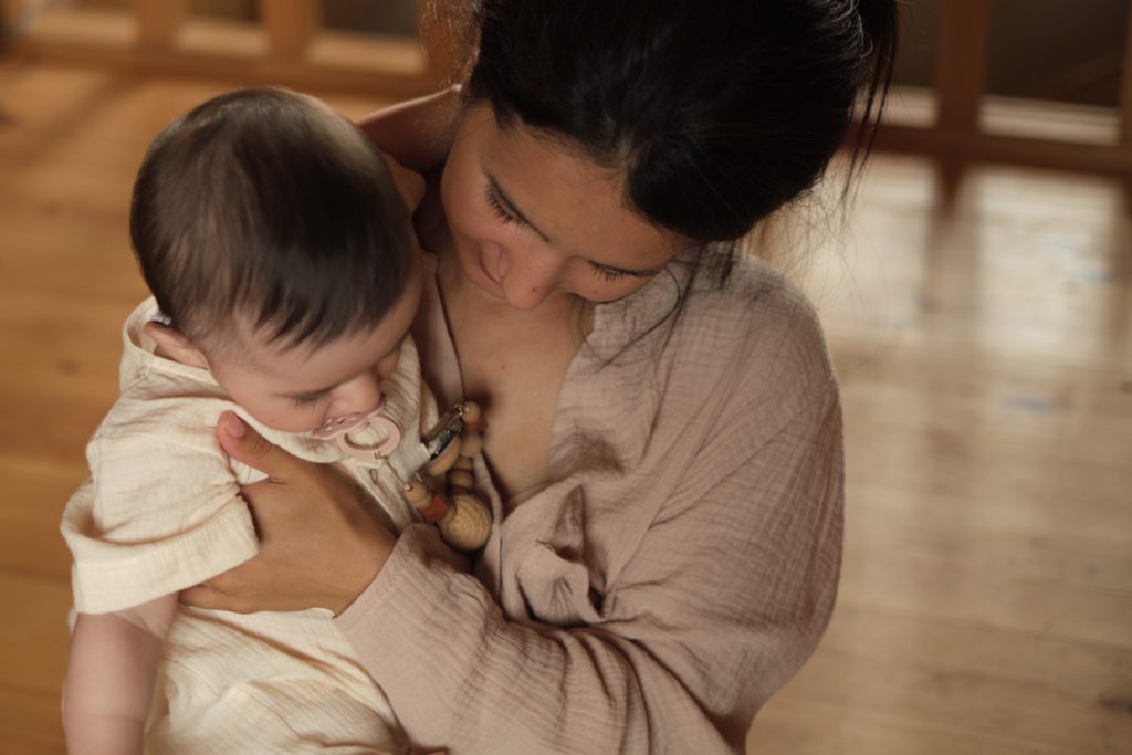 Mãe abraça e beija o bebê. O bebê está de costas, olhando para baixo.