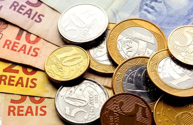 Notas e moedas do Real brasileiro de diversos valores, empilhadas e espalhadas.